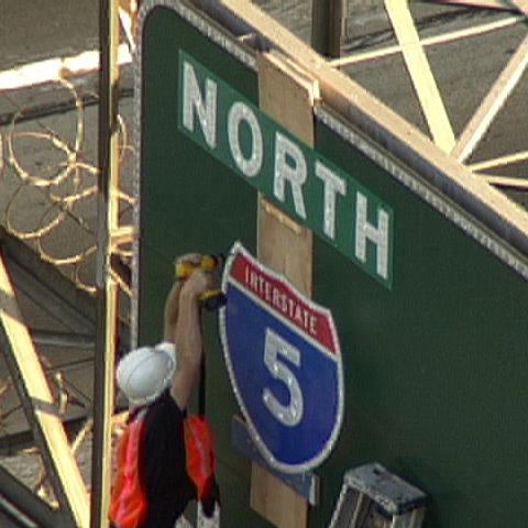 Artist disguised as a government construction worker alters a highway sign.